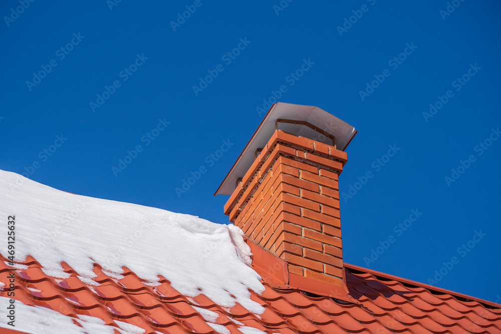 Red roof of a detached house and chimney and snow against the blue sky in winter