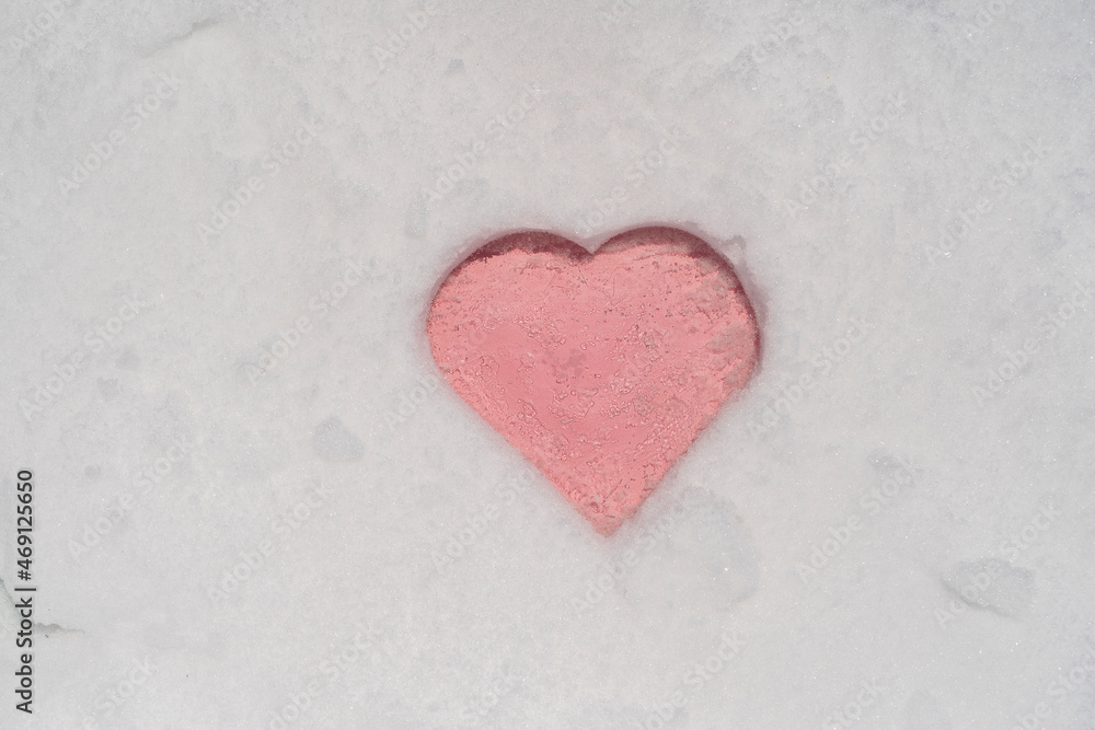 Pink heart shape on a white fresh snow in winter, close up
