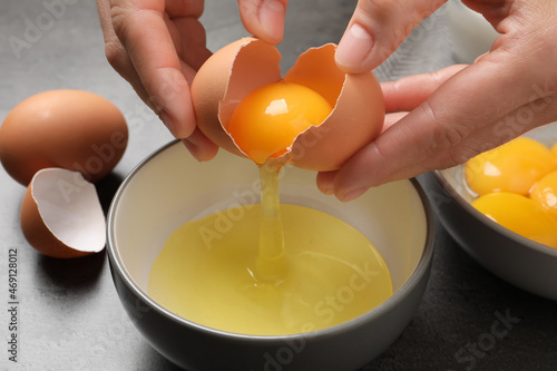 Woman separating egg yolk from white over bowl at grey table, closeup photo