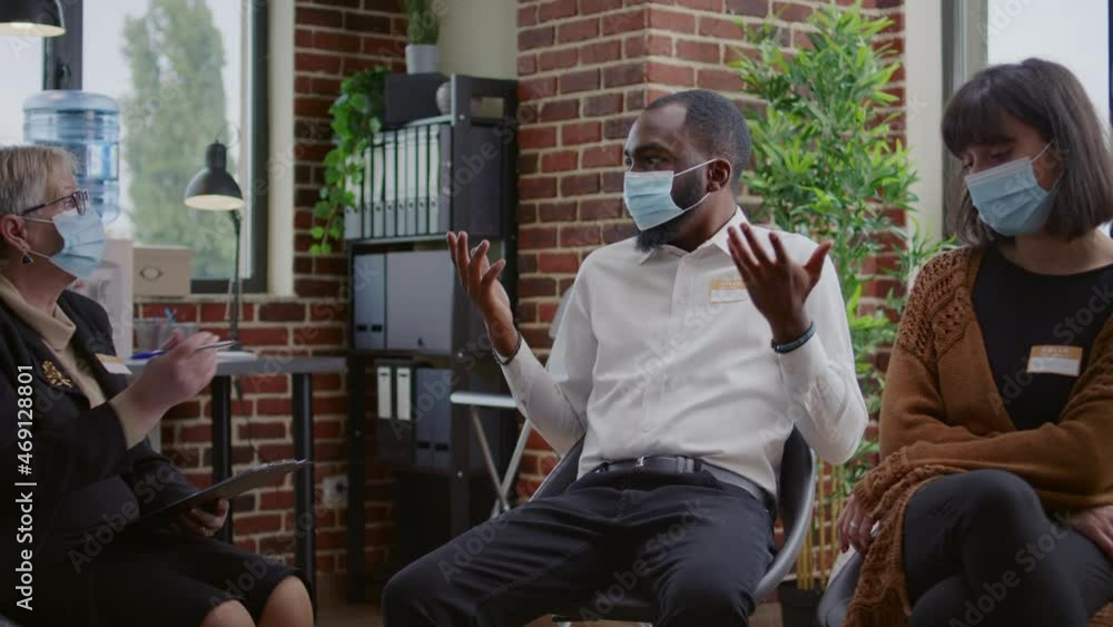 Desperate man sharing addiction issues with group and counselor at aa therapy session, wearing face mask. Adult having depression and mental health problems at rehabilitation meeting. Desperate man sharing addiction issues with group and counselor at aa therapy session, wearing face mask. Adult having depression and mental health problems at rehabilitation meeting.