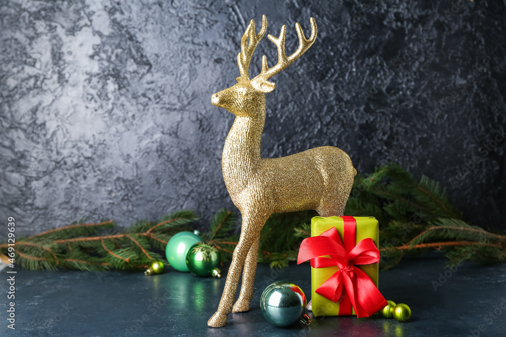 Golden reindeer with Christmas gift and balls on dark background