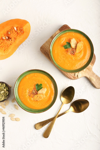 Bowls with delicious pumpkin cream soup and seeds on light background