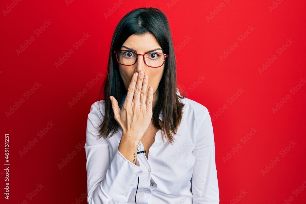 Young hispanic woman using lavalier microphone covering mouth with hand, shocked and afraid for mistake. surprised expression