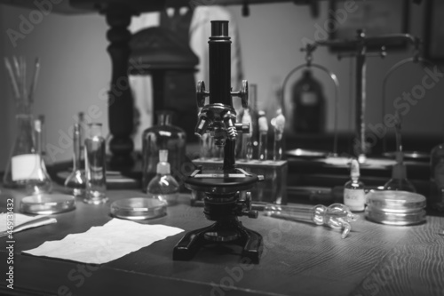 Vintage old microscope on table for science background. Medicine  alchemy  pharmacist. glass jars  flasks and tools  Selective focus. Black and white.