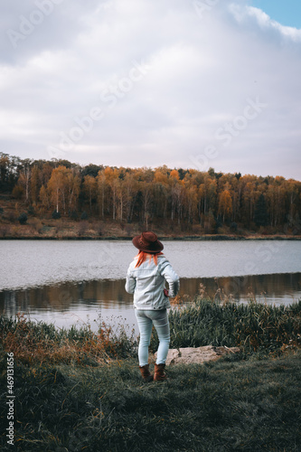 Girl, woman enjoying beauty of nature looking at lake. Adventure travel. Woman stands with leather hat on background with summer forest Vertical photo