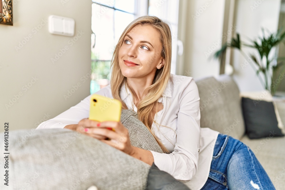 Young blonde woman using smartphone sitting on the sofa at home. Young blonde woman using smartphone sitting on the sofa at home.