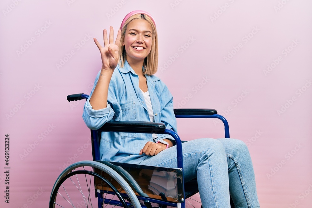 Beautiful blonde woman sitting on wheelchair showing and pointing up with fingers number four while smiling confident and happy. Beautiful blonde woman sitting on wheelchair showing and pointing up with fingers number four while smiling confident and happy.