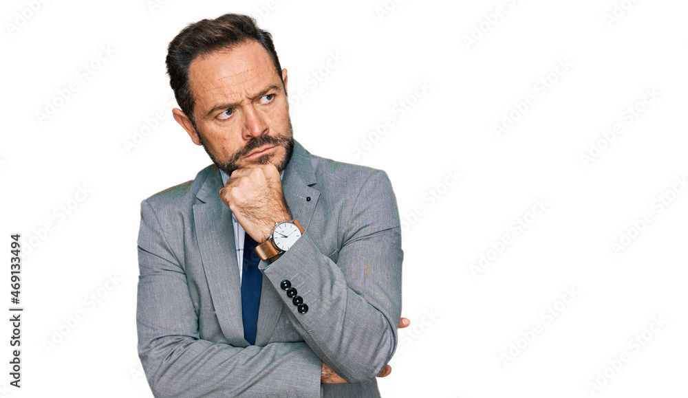Middle age man wearing business clothes with hand on chin thinking about question, pensive expression. smiling with thoughtful face. doubt concept. Middle age man wearing business clothes with hand on chin thinking about question, pensive expression. smiling with thoughtful face. doubt concept.