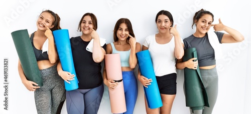 Group of women holding yoga mat standing over isolated background pointing with hand finger to face and nose  smiling cheerful. beauty concept