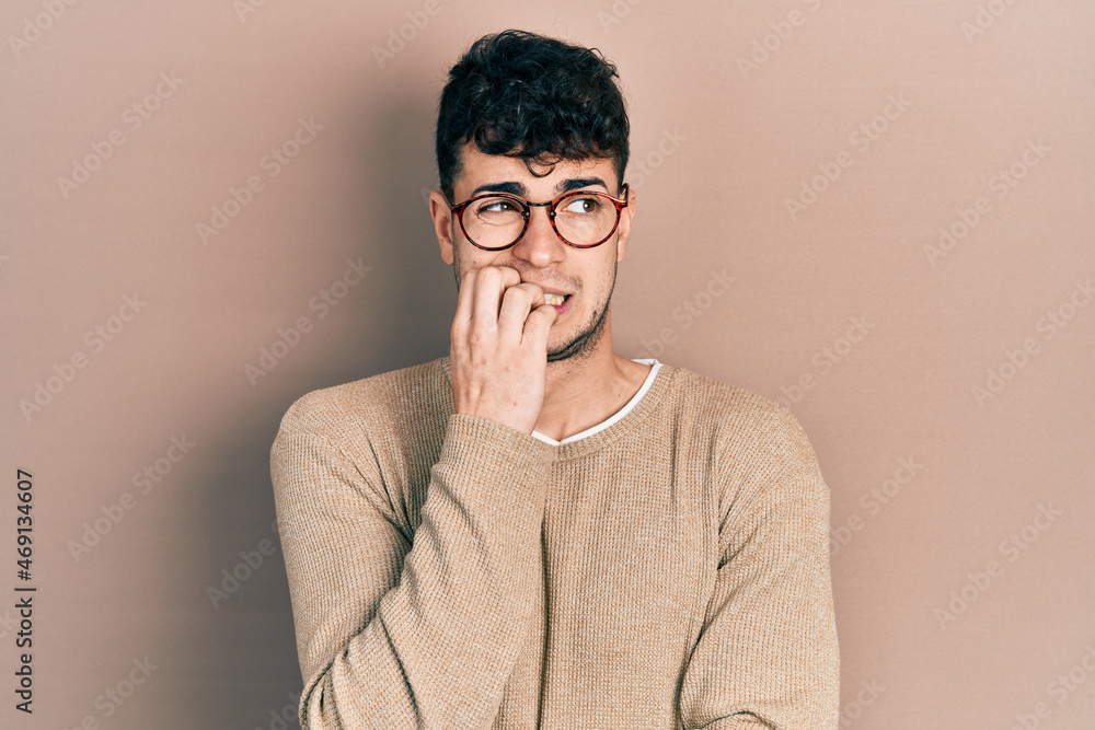 Young hispanic man wearing casual clothes and glasses looking stressed and nervous with hands on mouth biting nails. anxiety problem. Young hispanic man wearing casual clothes and glasses looking stressed and nervous with hands on mouth biting nails. anxiety problem.