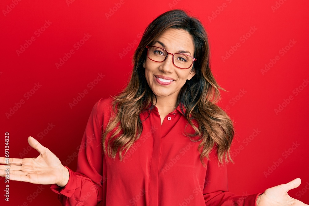 Young latin woman wearing casual clothes and glasses clueless and confused expression with arms and hands raised. doubt concept. Young latin woman wearing casual clothes and glasses clueless and confused expression with arms and hands raised. doubt concept.