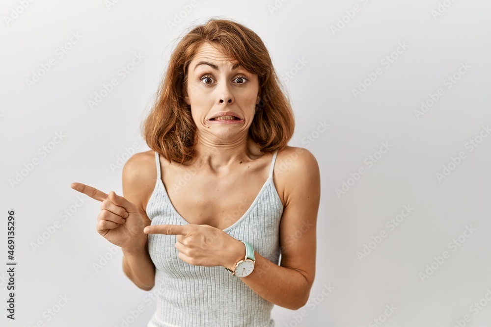 Beautiful caucasian woman standing over isolated background pointing aside worried and nervous with both hands, concerned and surprised expression Beautiful caucasian woman standing over isolated background pointing aside worried and nervous with both hands, concerned and surprised expression