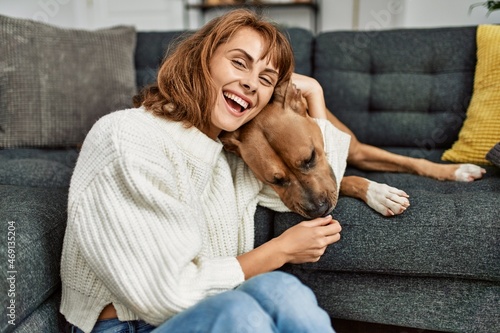 Young caucasian woman smiling confident hugging dog sitting on floor at home