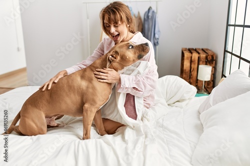 Fototapeta Naklejka Na Ścianę i Meble -  Young caucasian woman smiling confident playing with dog sitting on bed at bedroom