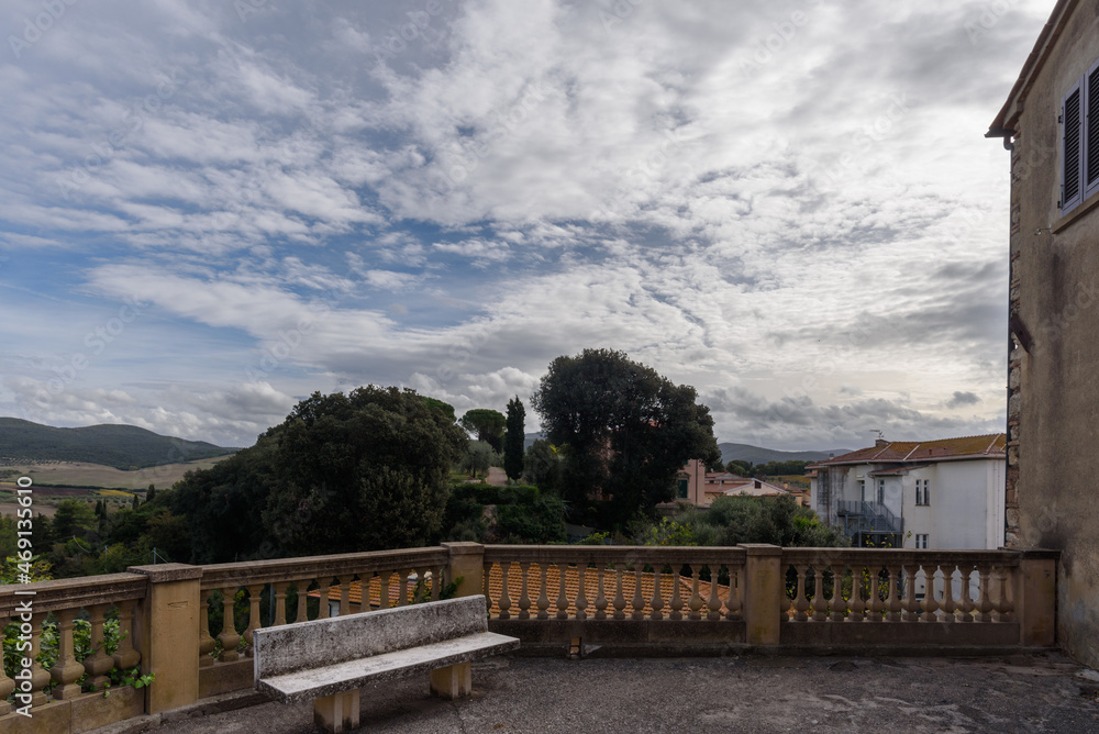 Blick auf die Macchia Malagona in Bibbona von Terrasse mit Bank bei Wolken und blauem Himmel im Gegenlicht