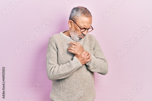 Handsome senior man with beard wearing casual sweater and glasses suffering pain on hands and fingers, arthritis inflammation © Krakenimages.com