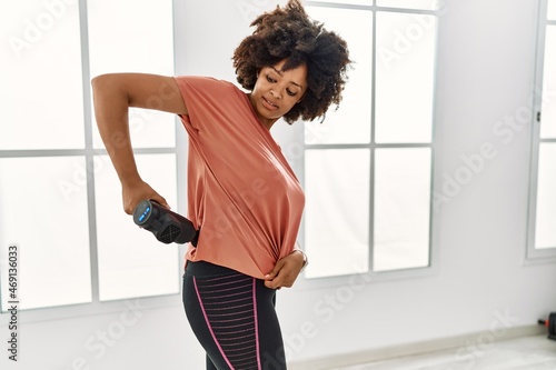 Young african american woman smiling confident using percussion pistol at sport center