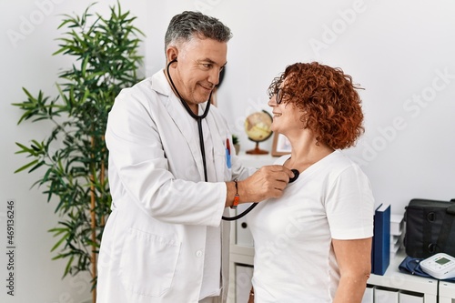 Middle age man and woman wearing doctor uniform auscultate heart having medical consultation at clinic photo