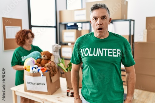 Middle age man wearing volunteer t shirt at donations stand afraid and shocked with surprise expression, fear and excited face.