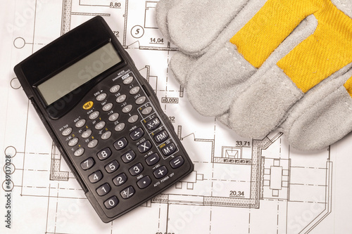 Planning the construction of a house. Construction gloves and calculator on the house plan.