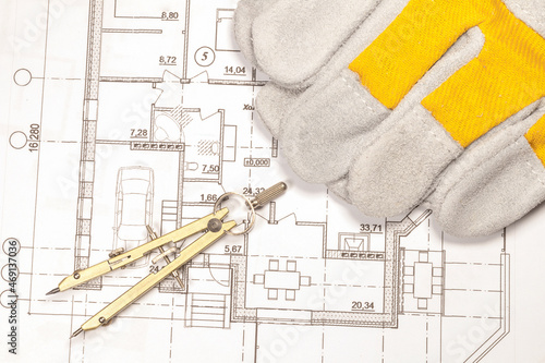 Calculation of the house according to the engineering plan. Work gloves and compasses are on the printed plan of the house.