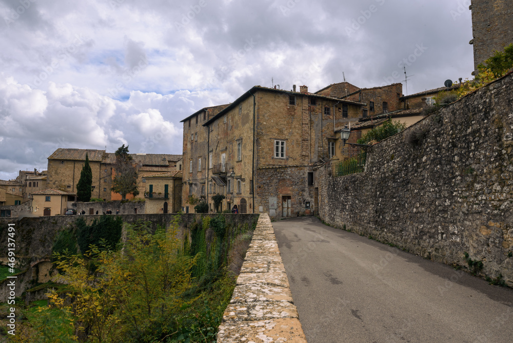 ausblick von Volterra auf die toskansiche Landscahft mit Himmel und Wolken und Gebäuden im Vordergrund und Straße mit Mauer