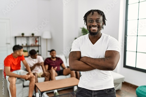 Young african man with friends at the living room happy face smiling with crossed arms looking at the camera. positive person.