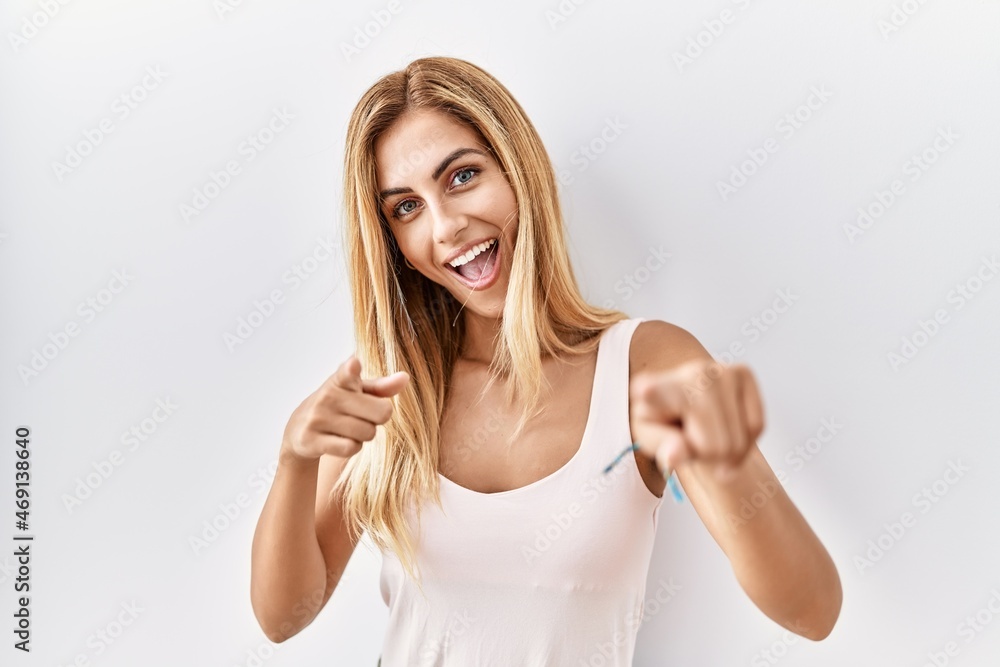 Blonde beautiful young woman standing over white isolated background pointing fingers to camera with happy and funny face. good energy and vibes. Blonde beautiful young woman standing over white isolated background pointing fingers to camera with happy and funny face. good energy and vibes.