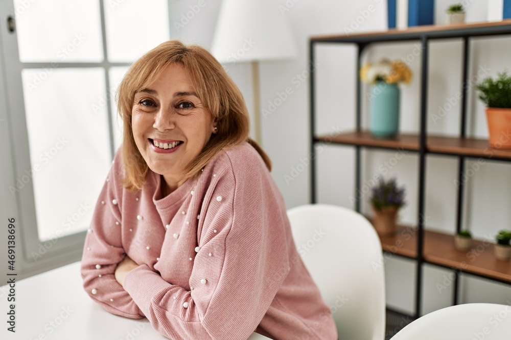 Middle age blonde woman smiling happy relaxed sitting on the table at home. Middle age blonde woman smiling happy relaxed sitting on the table at home.