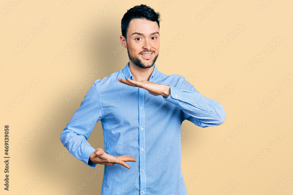 Hispanic man with beard wearing casual business shirt gesturing with hands showing big and large size sign, measure symbol. smiling looking at the camera. measuring concept. Hispanic man with beard wearing casual business shirt gesturing with hands showing big and large size sign, measure symbol. smiling looking at the camera. measuring concept.