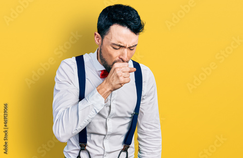 Hispanic man with beard wearing hipster look with bow tie and suspenders feeling unwell and coughing as symptom for cold or bronchitis. health care concept.