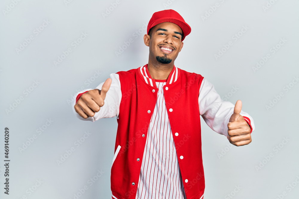 Young african american man wearing baseball uniform approving doing positive gesture with hand, thumbs up smiling and happy for success. winner gesture. Young african american man wearing baseball uniform approving doing positive gesture with hand, thumbs up smiling and happy for success. winner gesture.