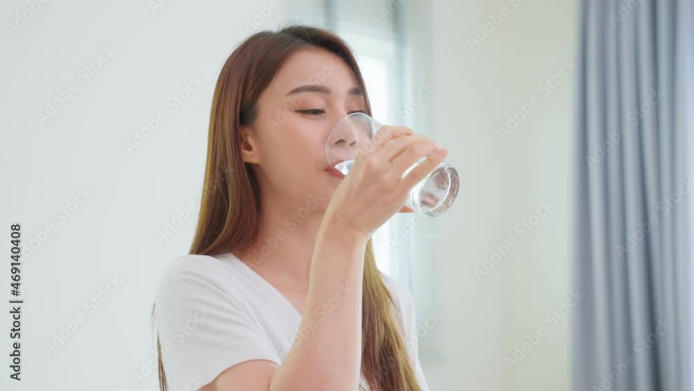 Asian attractive woman sit on bed, drink a glass of water in bedroom. Asian attractive woman sit on bed, drink a glass of water in bedroom.