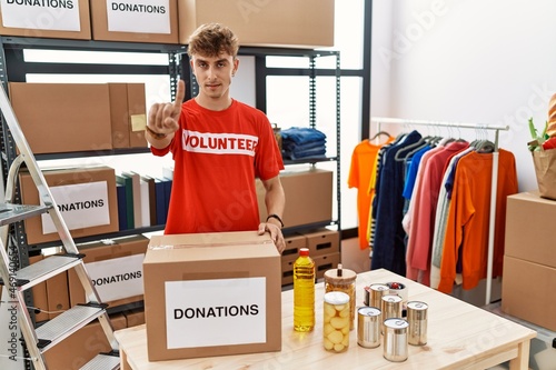 Young caucasian man volunteer holding donations box pointing with finger up and angry expression, showing no gesture