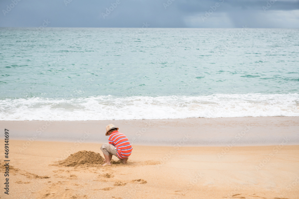 Asian boy with hat make sand castle at beach, Phuket Asian boy with hat make sand castle at beach, Phuket