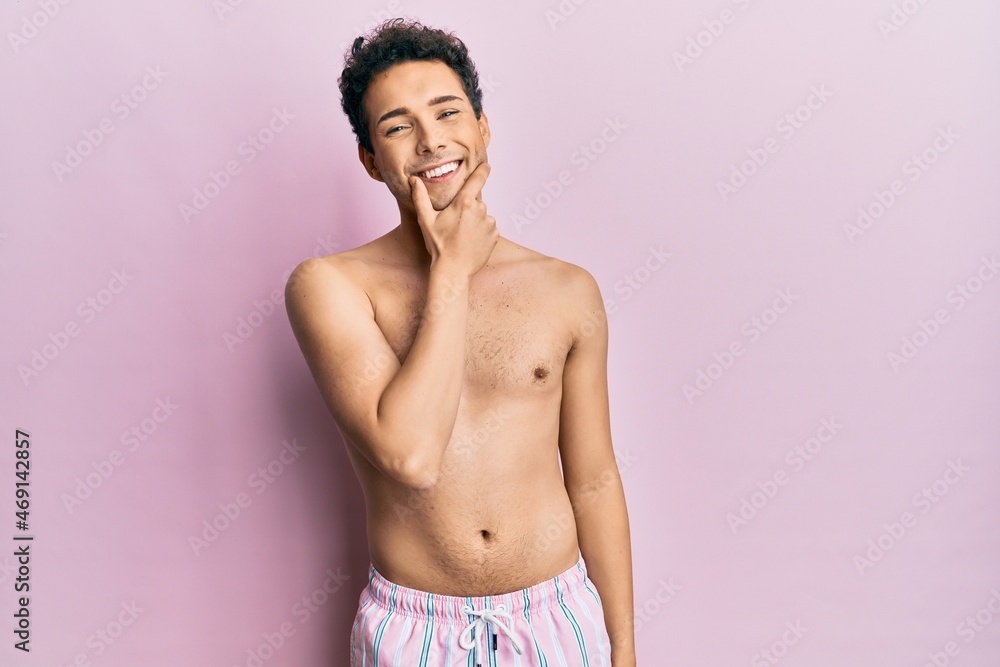 Fototapeta premium Young handsome man wearing swimwear shirtless looking confident at the camera smiling with crossed arms and hand raised on chin. thinking positive.