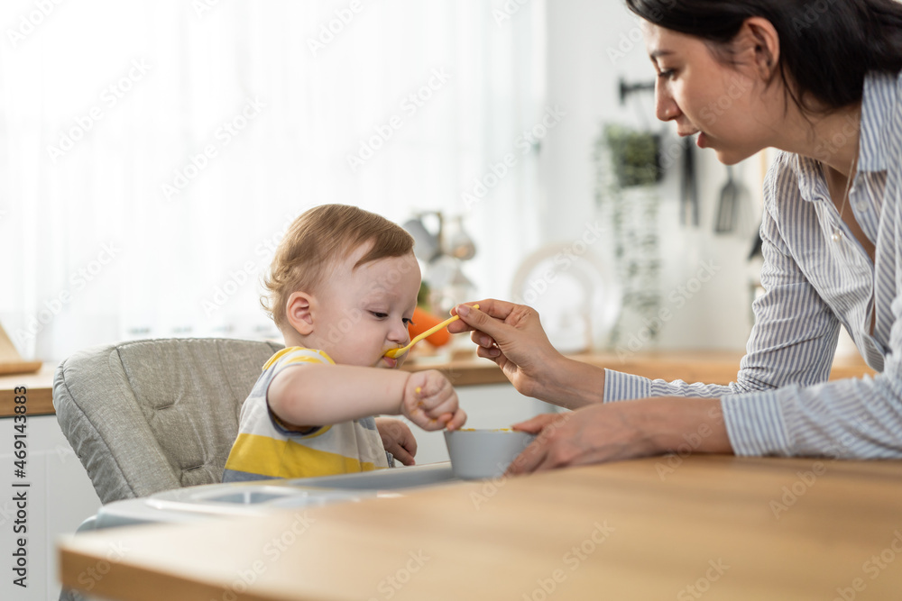 Caucasian beautiful mother take care of baby boy toddler in kitchen. Caucasian beautiful mother take care of baby boy toddler in kitchen.