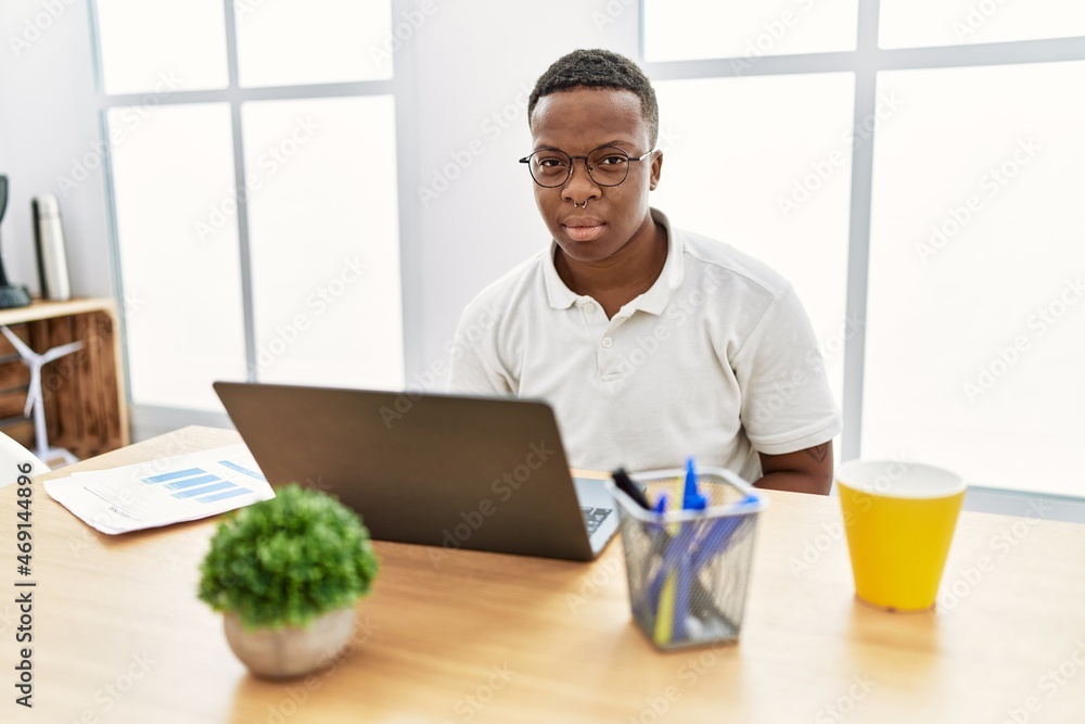 Young african man working at the office using computer laptop relaxed with serious expression on face. simple and natural looking at the camera. Young african man working at the office using computer laptop relaxed with serious expression on face. simple and natural looking at the camera.