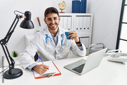 Handsome hispanic man working as doctor drinking a coffee at medical consultation