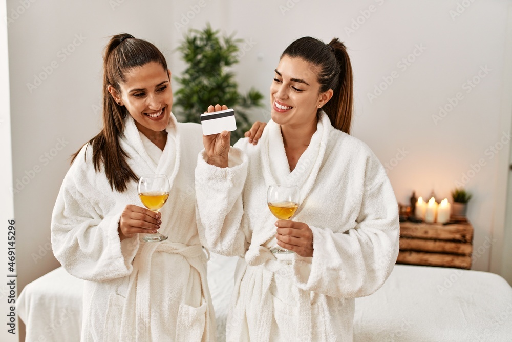 Two women holding credit card toasting with champagne standing at beauty center Two women holding credit card toasting with champagne standing at beauty center