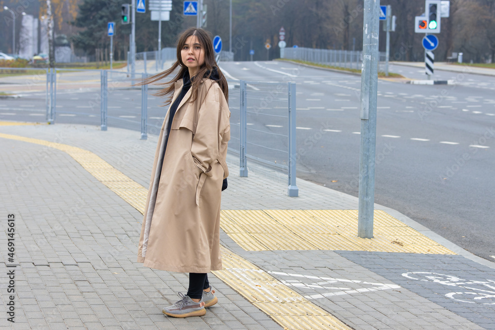 A beautiful girl in a long coat stands on a deserted city street