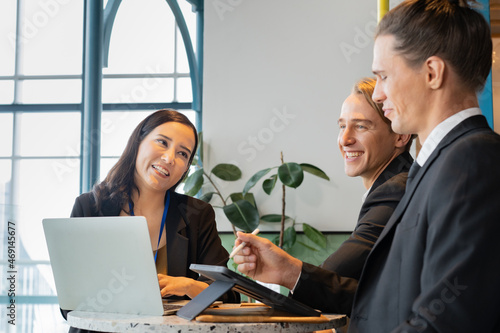 A happy group of business people, Asian businesswoman and Caucasian businessmen sitting at a round table with laptop and tablet, having a business conversation during the small conference in a cafe.