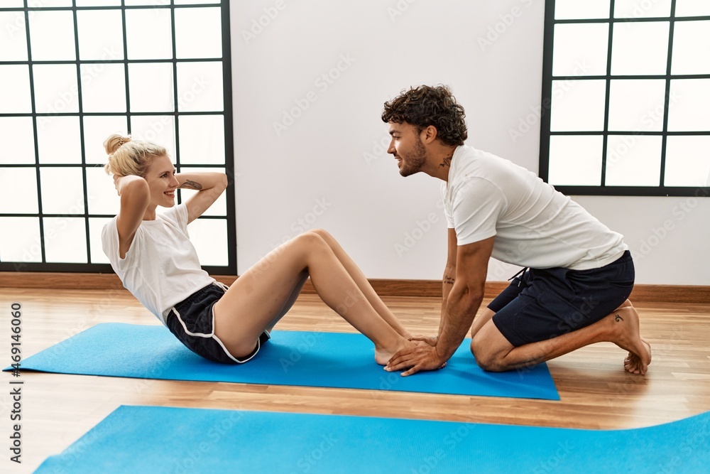 Young couple smiling happy training abs exercise at sport center.