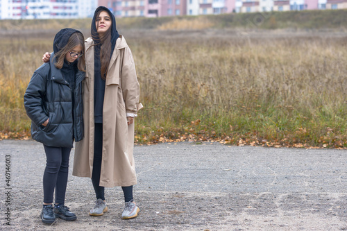 Two girls in autumn clothes stand together on a deserted outskirts of the city