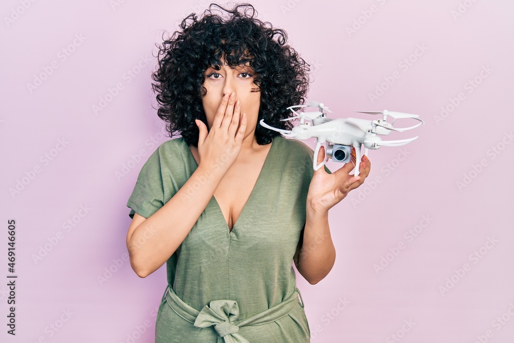 Obraz premium Young middle east woman holding drone covering mouth with hand, shocked and afraid for mistake. surprised expression