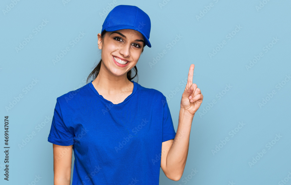 Young hispanic girl wearing delivery courier uniform showing and pointing up with finger number one while smiling confident and happy.