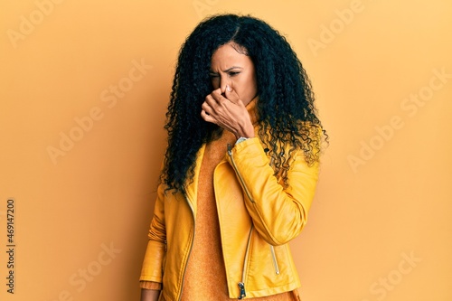 Middle age african american woman wearing wool winter sweater and leather jacket smelling something stinky and disgusting, intolerable smell, holding breath with fingers on nose. bad smell