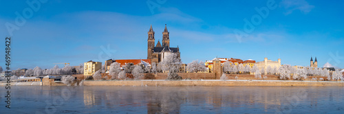 Panoramic view over Magdeburg historical downtown in Winter with icy trees and snow during sunrise in the morning with warm illumination, foggy river and blue sky, Germany.