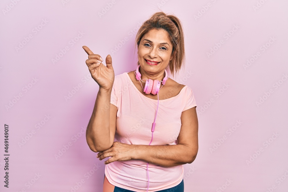 Middle age hispanic woman wearing gym clothes and using headphones smiling happy pointing with hand and finger to the side Middle age hispanic woman wearing gym clothes and using headphones smiling happy pointing with hand and finger to the side
