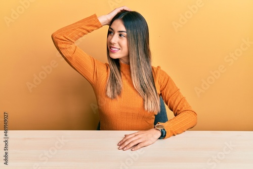 Young hispanic woman wearing casual clothes sitting on the table smiling confident touching hair with hand up gesture, posing attractive and fashionable © Krakenimages.com